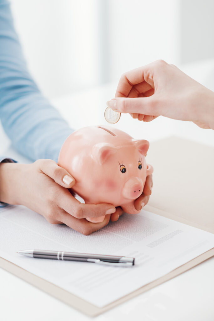 Mains déposant une pièce dans une tirelire en forme de cochon, symbolisant l’épargne et la gestion financière optimisée pour les entreprises